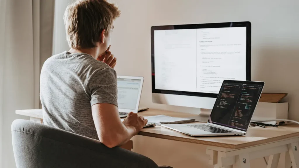 Coder using Claude AI for programming assistance on multiple screens, showcasing a modern home office setup for efficient software development.